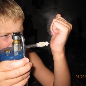 A boy is smoking an electronic cigarette and holding a device.